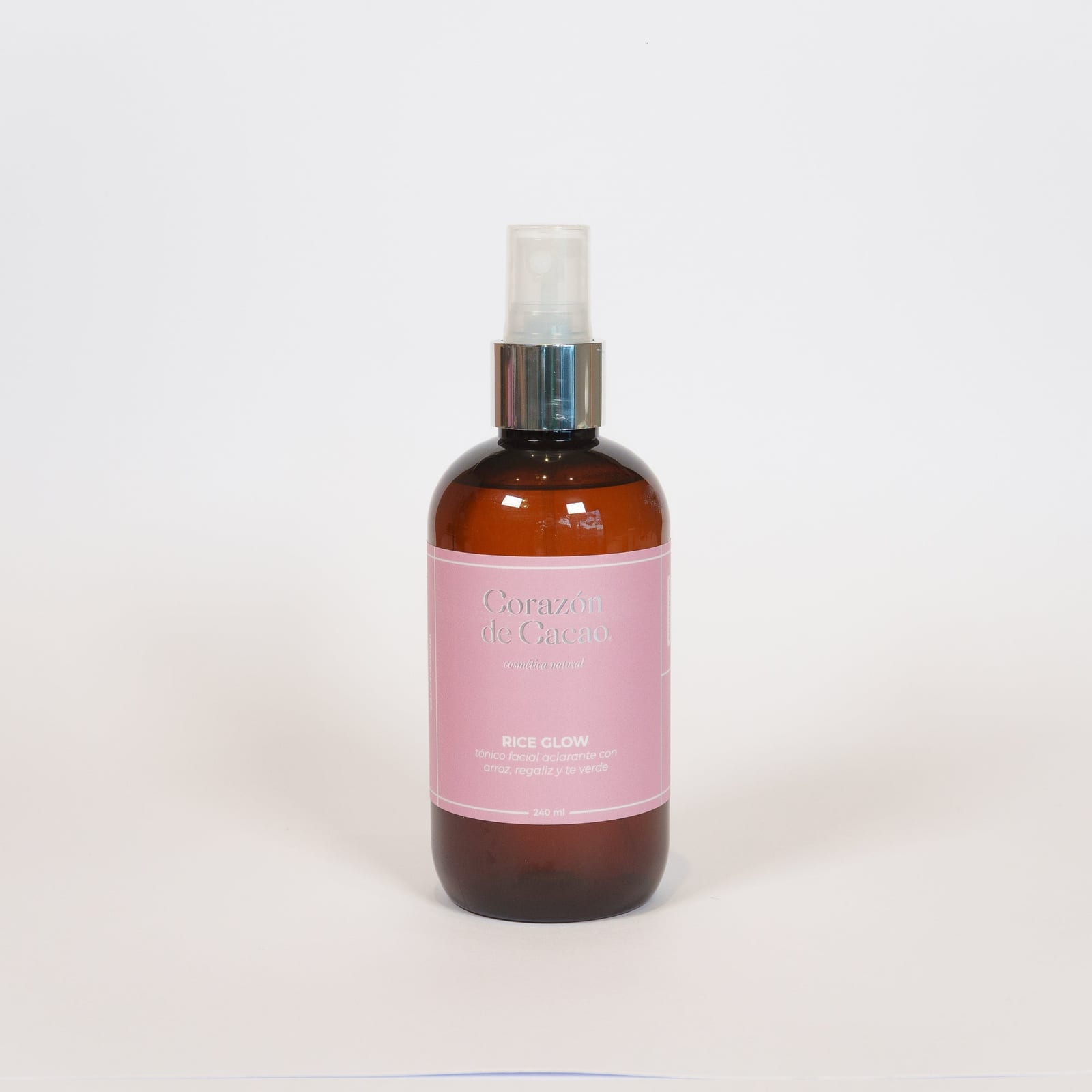 Frasco ámbar con atomizador del tónico Rice Glow de Corazón de Cacao, con etiqueta rosa, sobre fondo blanco