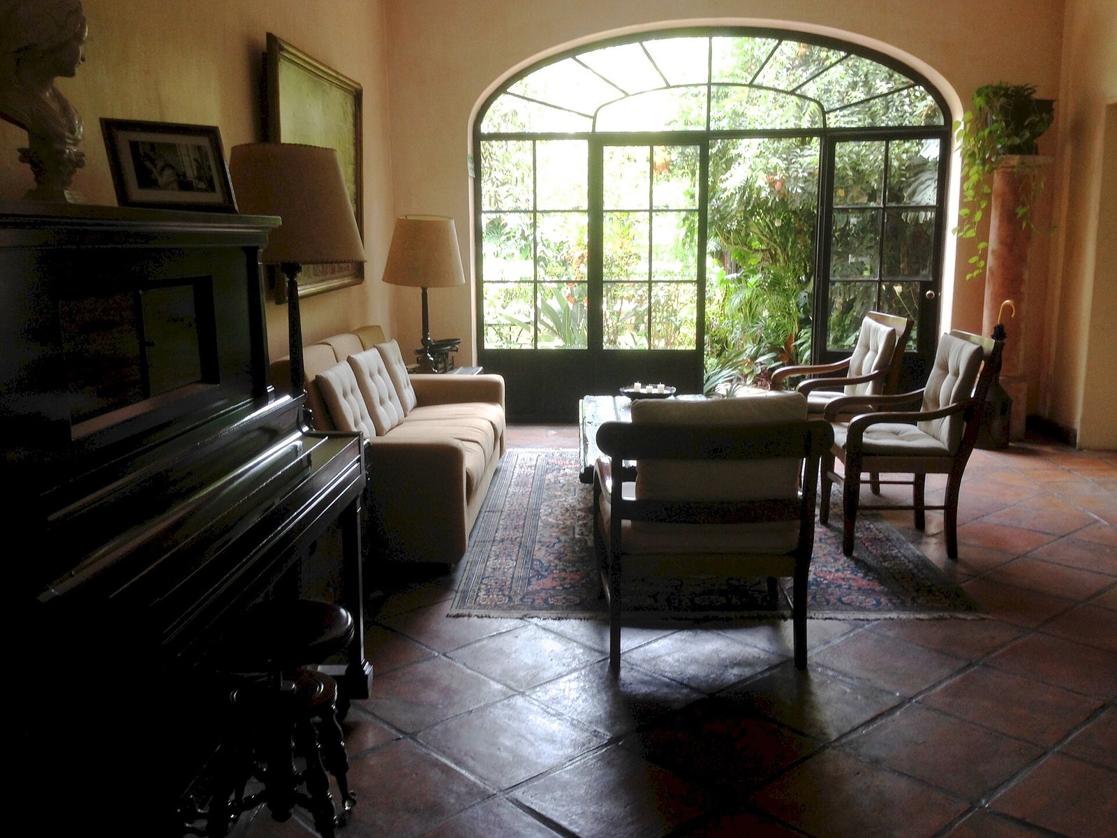 Sala de Villa Ganz con piano, sillones y un ventanal en arco que da al jardín