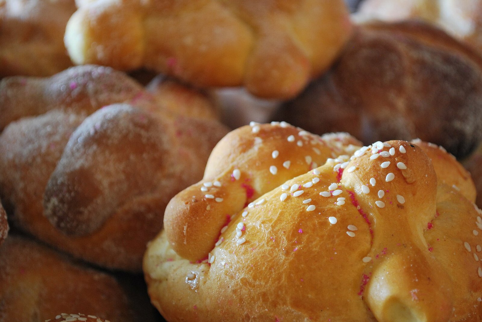 Piezas de pan de muerto con ajonjolí y azúcar, apiladas una junto a otra