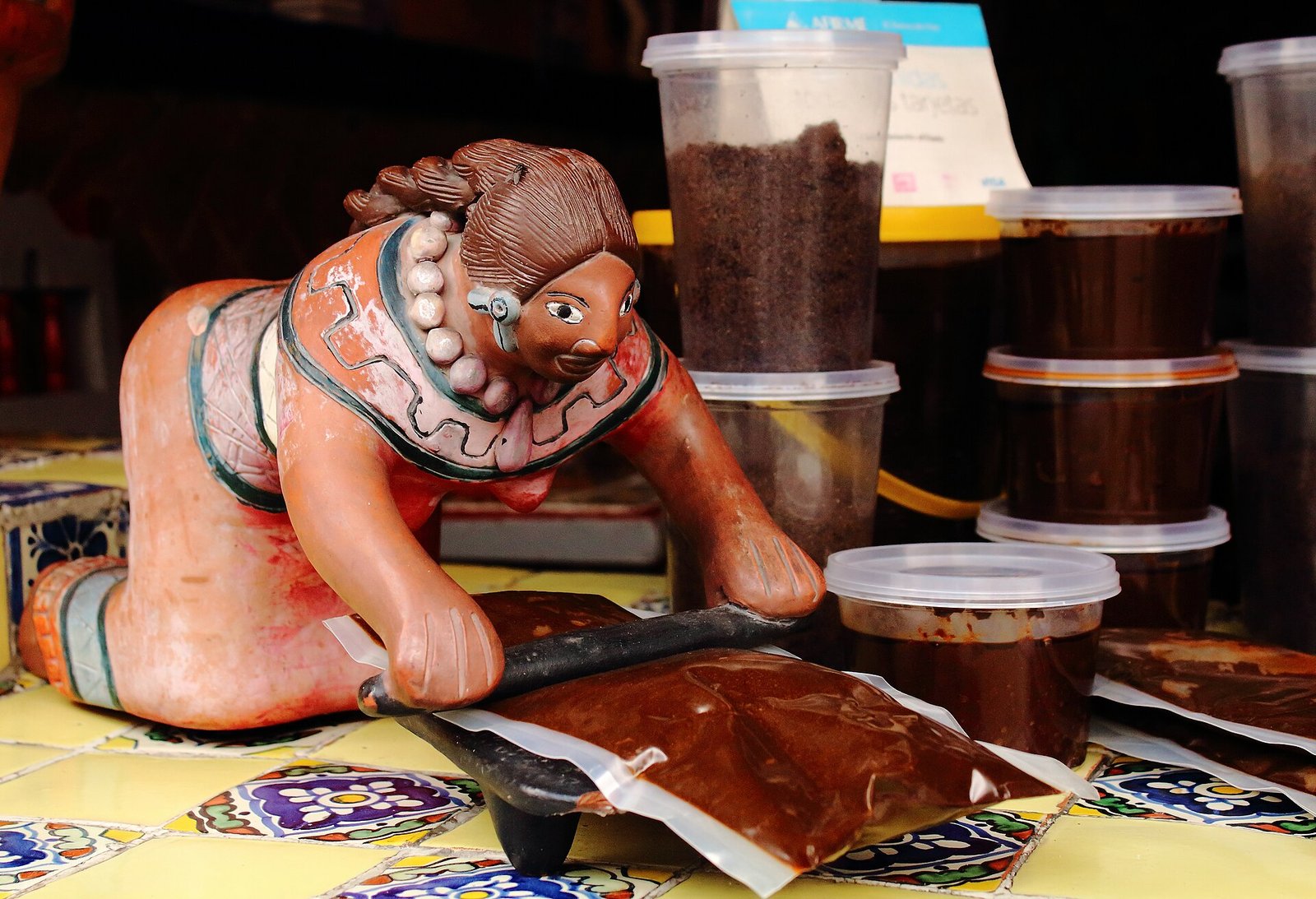 Mole poblano en pasta y en polvo a la venta en Puebla, junto a una figura de barro que muele en un metate