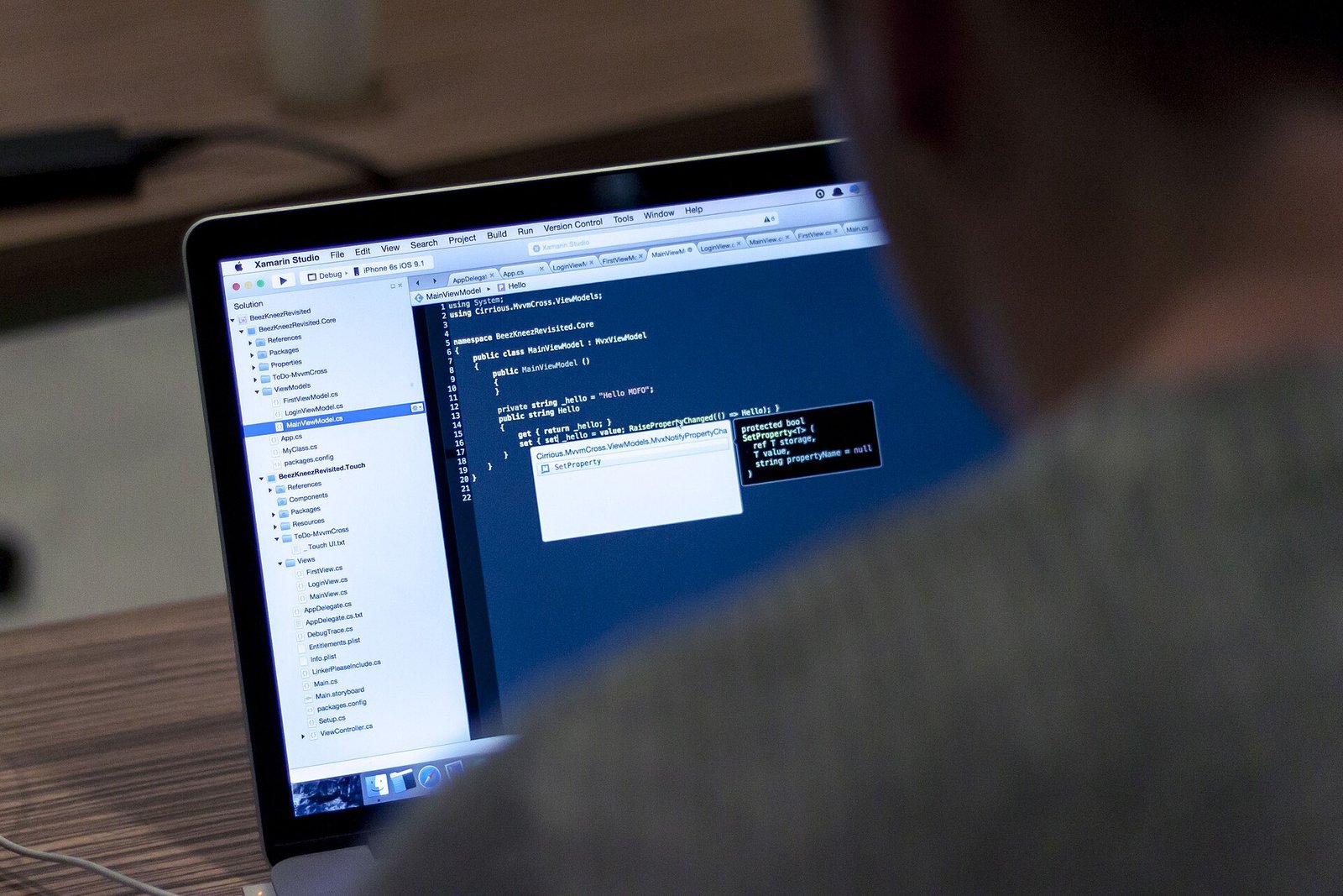 Persona de espaldas frente a una laptop con código de programación en pantalla