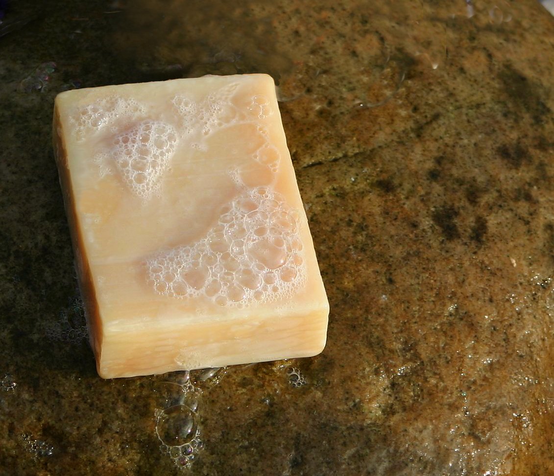 Barra de jabón artesanal con espuma sobre una piedra mojada