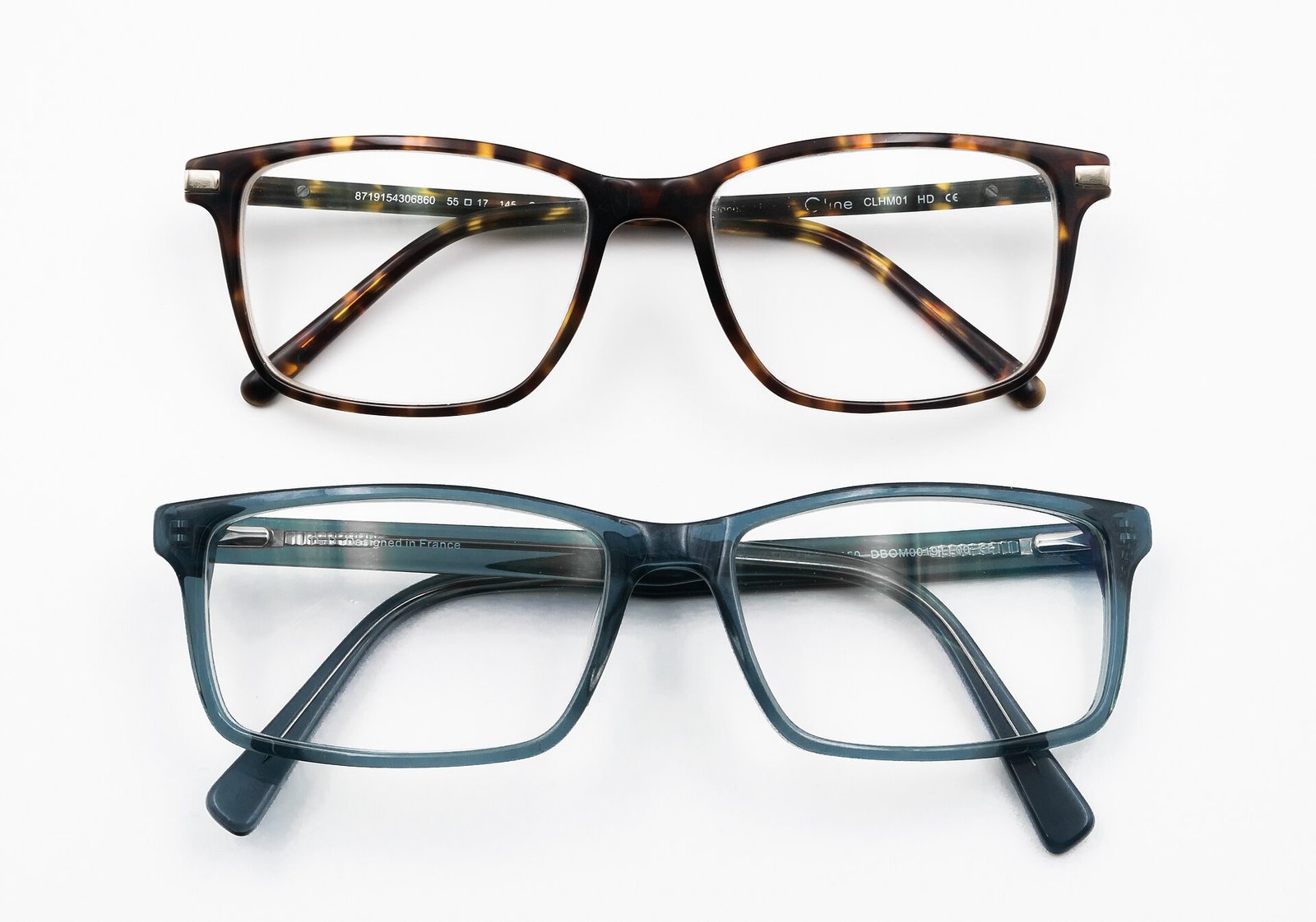 Dos armazones de lentes oftálmicos, uno de carey y otro azul translúcido, sobre fondo blanco