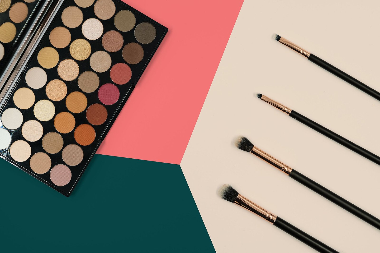 Paleta de sombras de ojos con tonos neutros y cuatro brochas de maquillaje sobre un fondo de colores