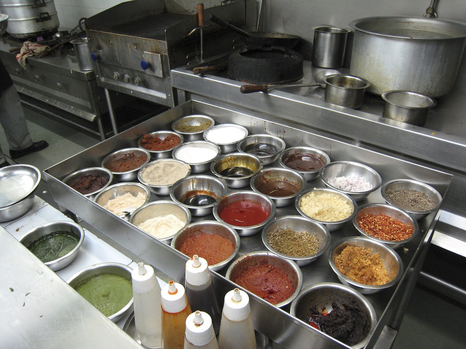 Recipientes de acero con salsas, especias e ingredientes listos junto a la estufa de una cocina profesional
