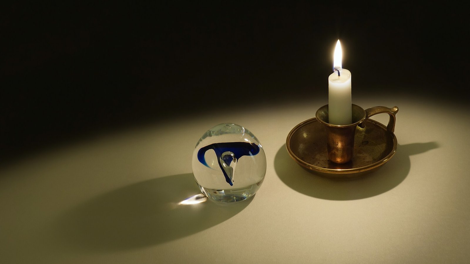 Vela encendida en un candelero de latón junto a un pisapapeles de vidrio