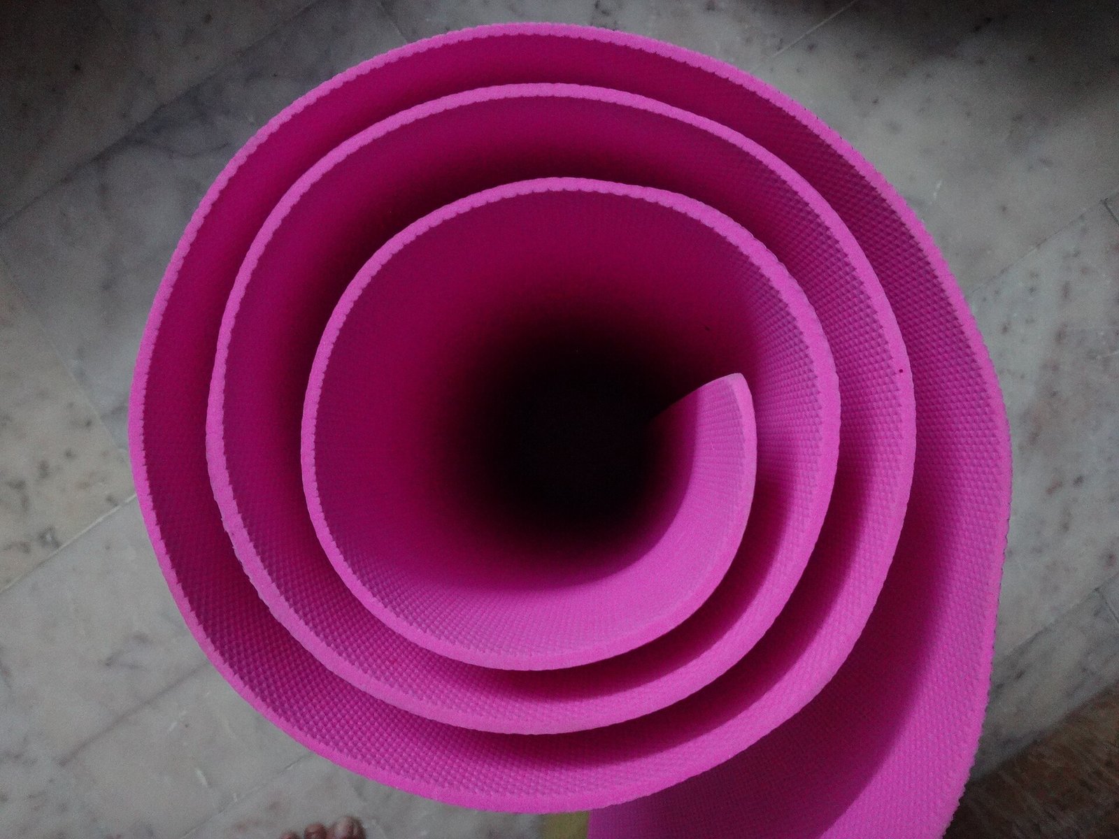 Tapete de yoga color rosa enrollado, visto desde arriba sobre un piso de mármol