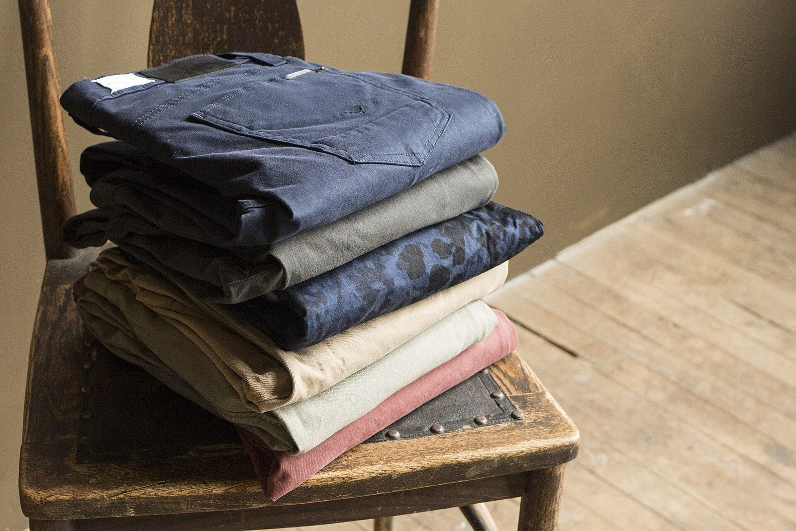 Pila de pantalones de gabardina doblados sobre una silla de madera
