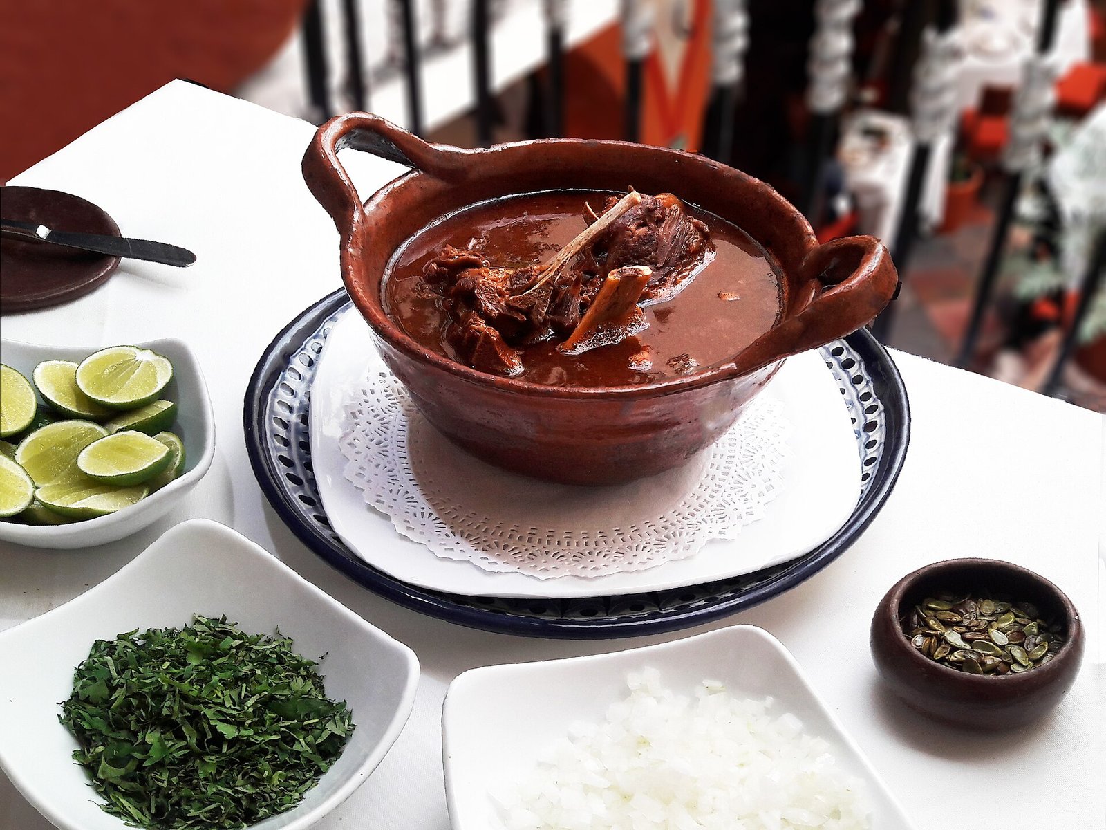 Cazuela de barro con mole de caderas, servida con limones, hierbas picadas, cebolla y semillas en platos aparte