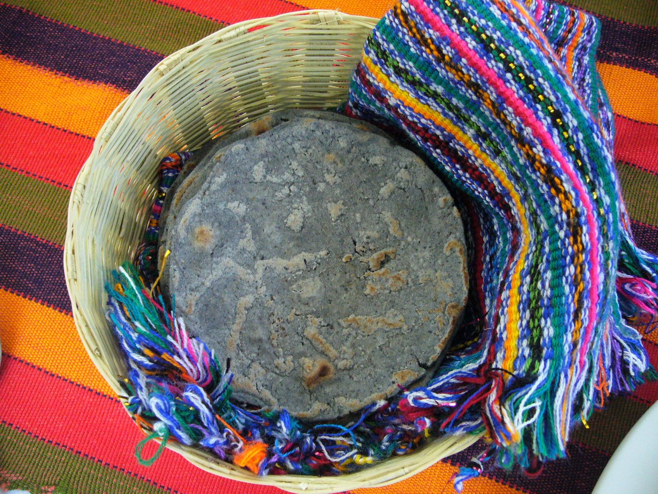 Tortilla de maíz azul en un tortillero de palma con una servilleta tejida de colores