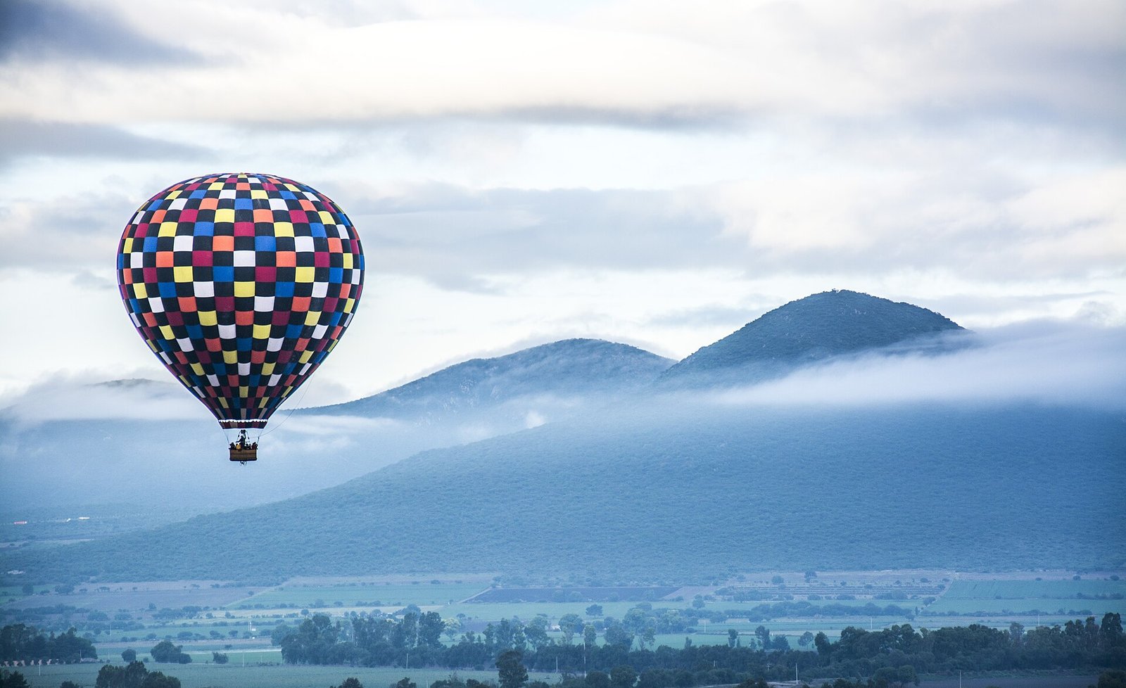 Globo aerostático de cuadros de colores sobre campos y cerros cubiertos de niebla en Tequisquiapan, Querétaro