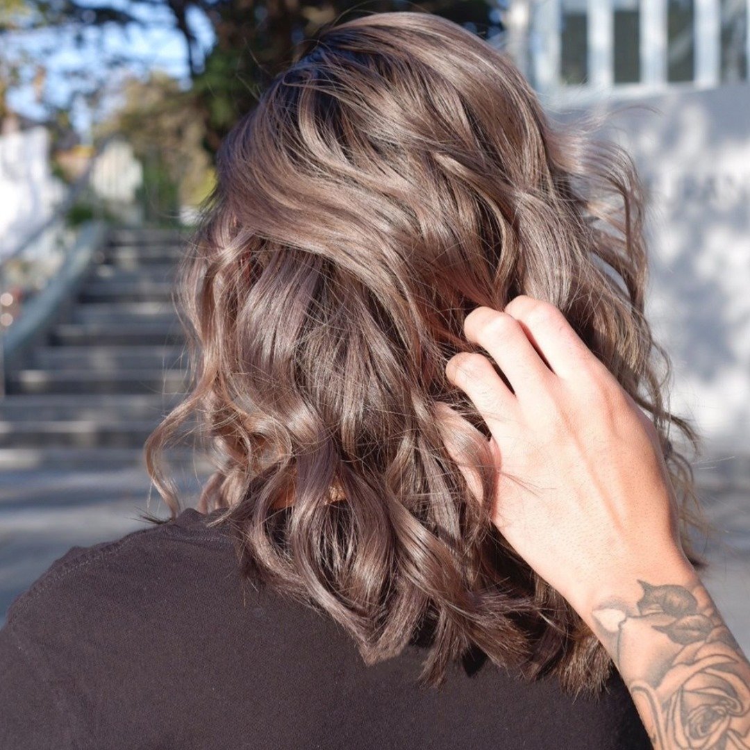 Cabello ondulado castaño visto de espaldas, con una mano acomodando las ondas