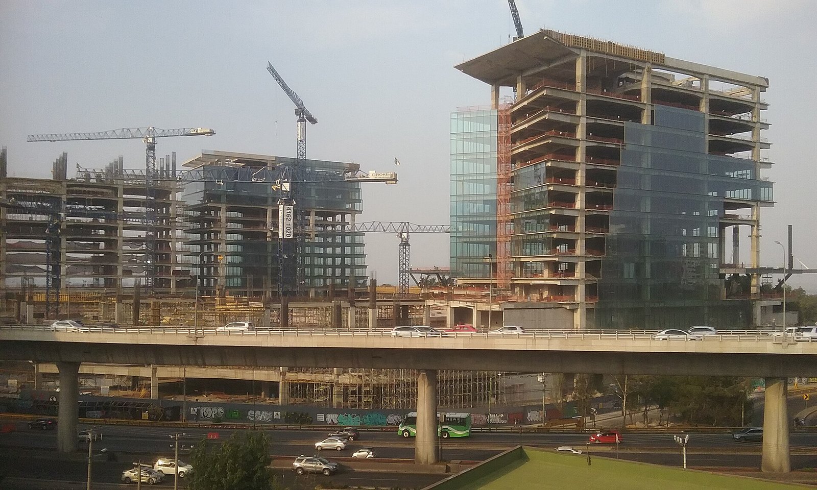 Edificios de oficinas en construcción, con grúas, junto a una vía elevada en la Ciudad de México