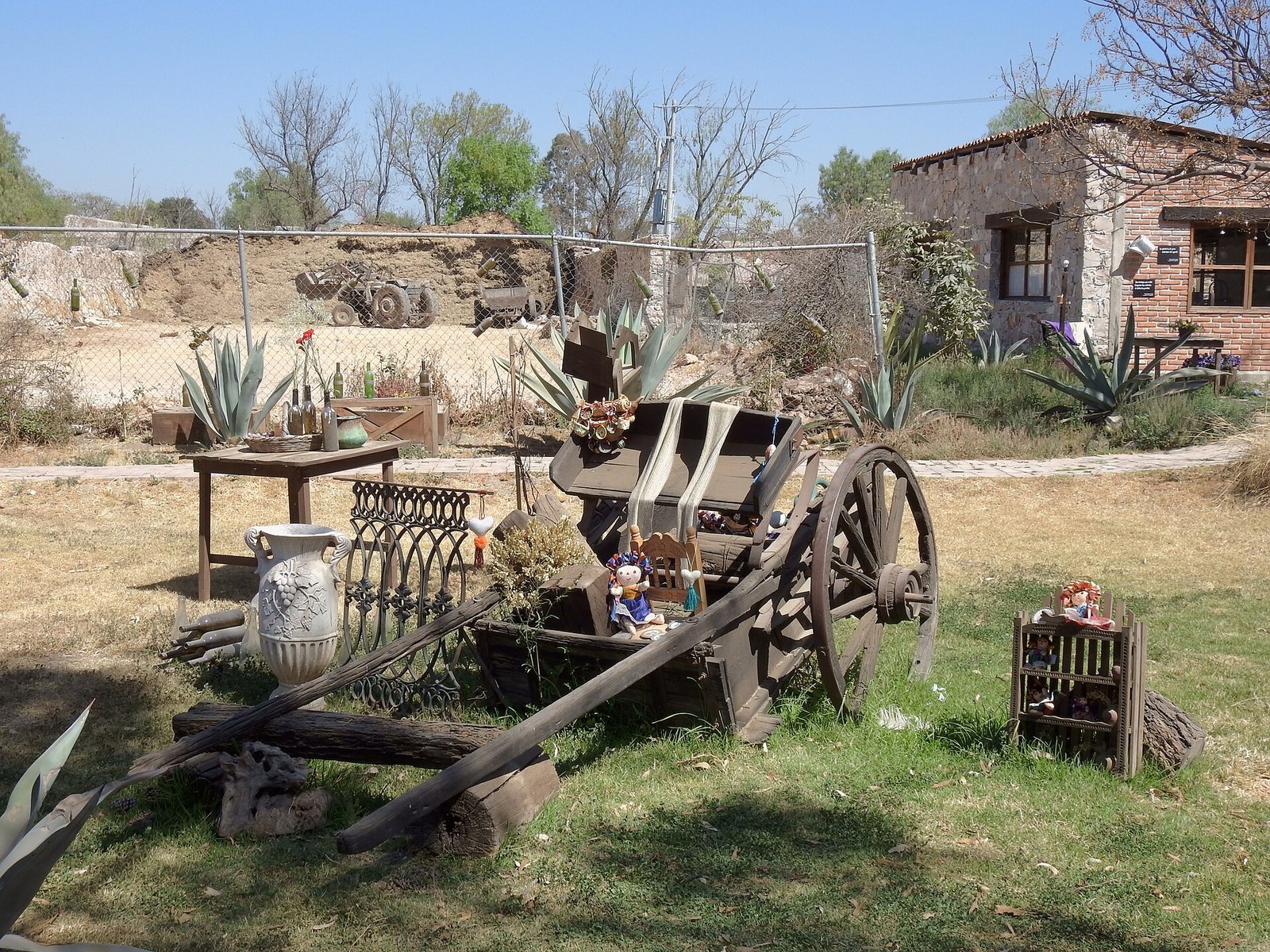 Carreta de madera con una muñeca y objetos decorativos sobre el pasto en los jardines de Quesos VAI, en Colón, Querétaro