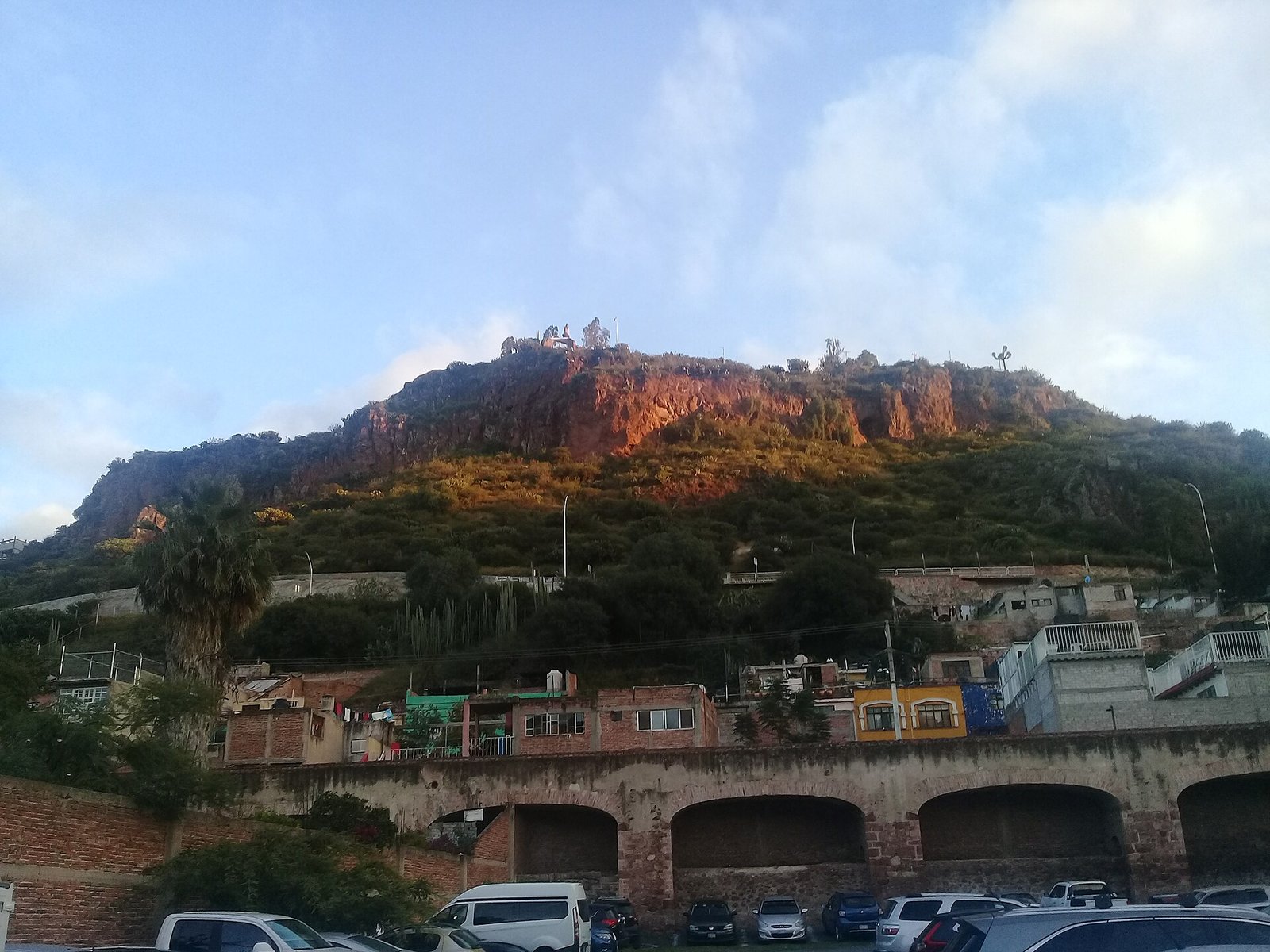 Arcos del acueducto de la antigua fábrica textil El Hércules, con casas y un cerro rojizo al fondo, en Querétaro
