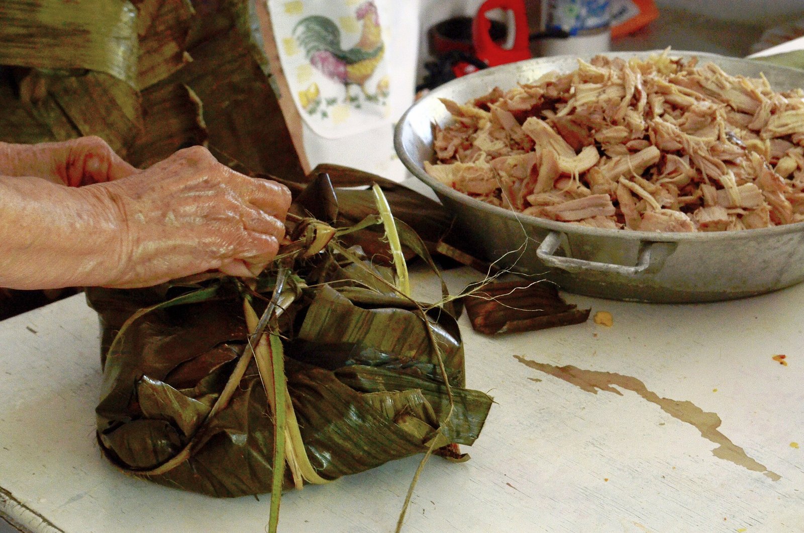 Manos envuelven en hojas de plátano un pib durante su preparación en Yucatán, junto a un recipiente con carne deshebrada