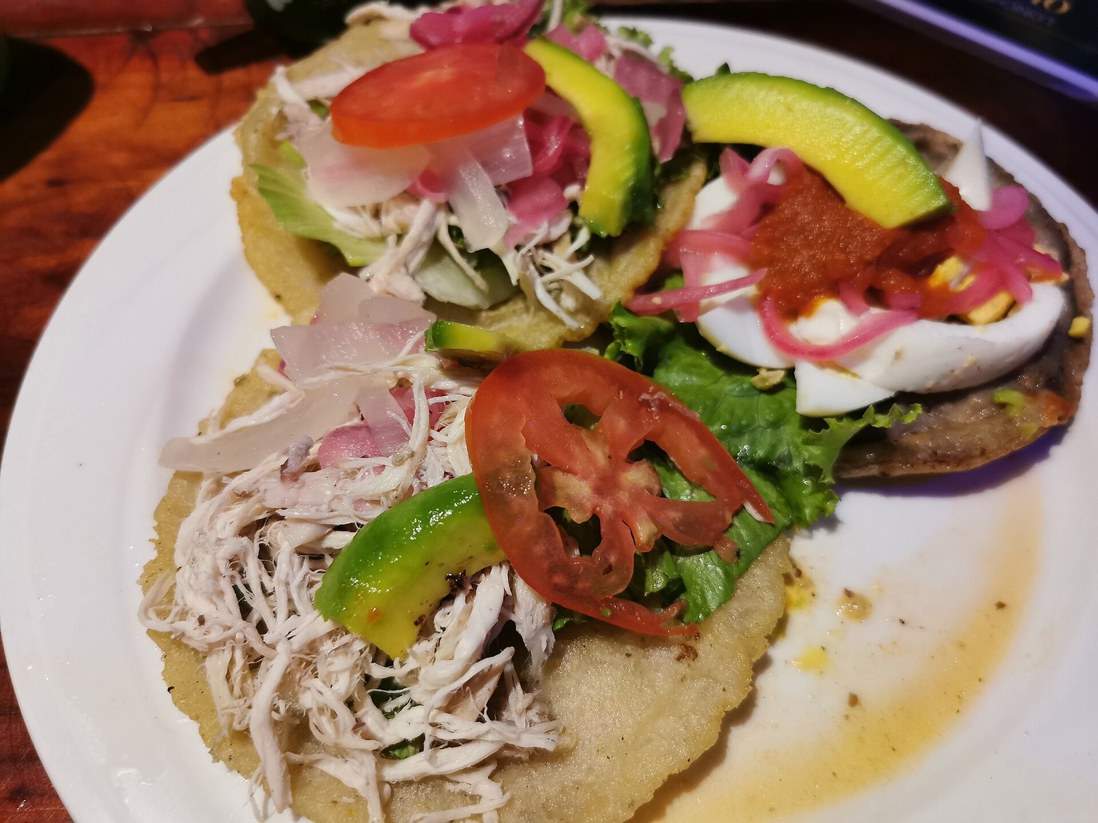 Plato con panuchos y salbutes cubiertos de pollo deshebrado, aguacate, jitomate, huevo y cebolla morada