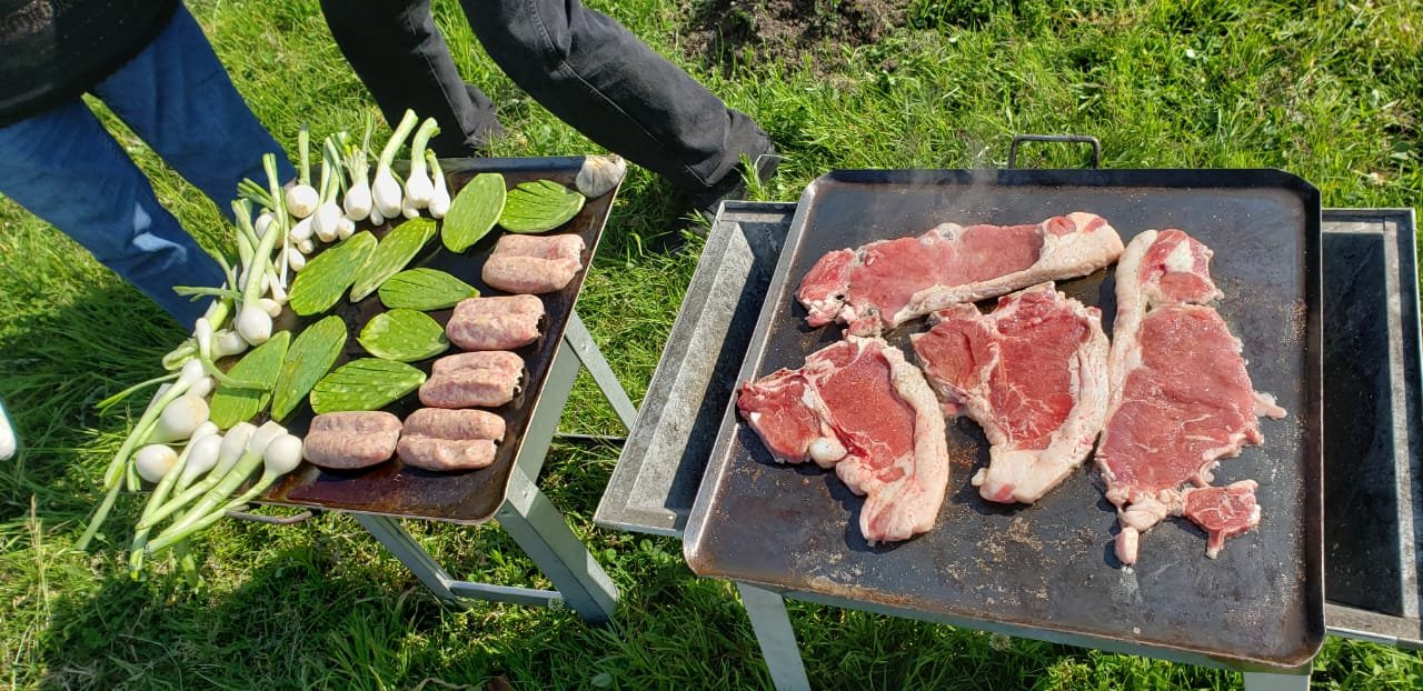 Cortes de carne, chorizos, cebollas y nopales sobre planchas de un asador al aire libre