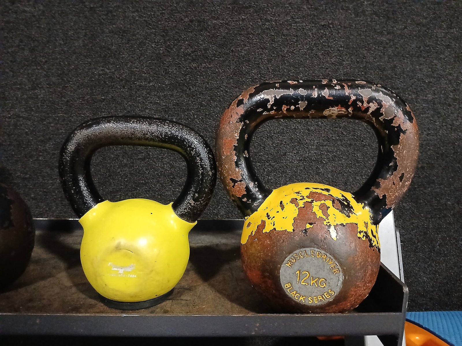 Dos pesas rusas, una amarilla y otra de hierro desgastado, sobre un estante de gimnasio